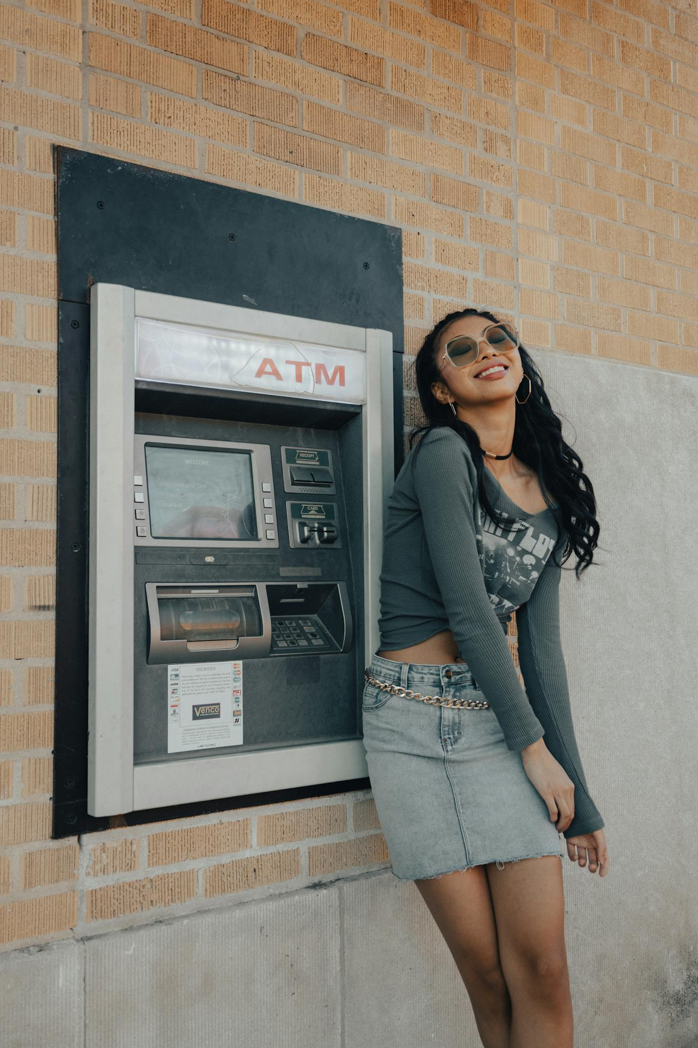 Fashionable woman posing near an ATM, showcasing urban lifestyle and modern fashion.