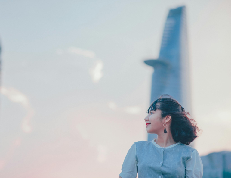 Portrait of a smiling woman in front of the Ho Chi Minh City skyline at sunset.